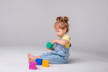 little baby girl is sitting on a white background and playing with colorful cubes. kid's play toy cubes
