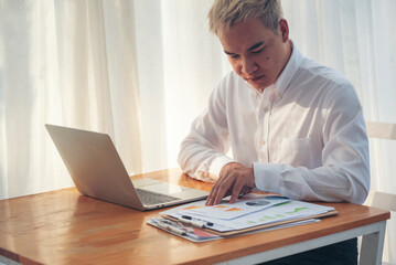 Fototapeta premium Asian Businessman type keyboard write financial graph chart Planning marketing data. Man hands using laptop at office desk reading spreadsheet excel finance document. Business men working home office
