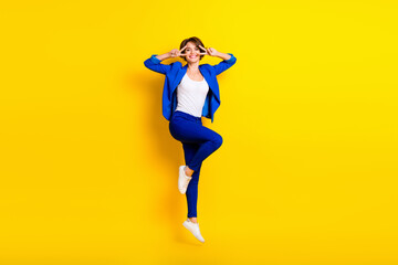 Fototapeta na wymiar Full length photo of sweet shiny woman wear blue jacket showing v-signs cover eyes jumping high isolated yellow color background