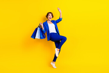 Fototapeta na wymiar Full length photo of cute impressed woman wear blue jacket having fun rising shoppers isolated yellow color background