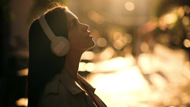 Half length profile portrait of young handsome caucasian woman listening music with headphones in the city at sunset