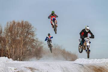 group of motorcyclists jump on hill winter motocross