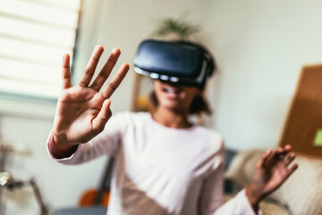 African American girl using virtual reality glasses in her room. Black girl enjoys VR technology to watch 3D movies or immerse herself in metaverse