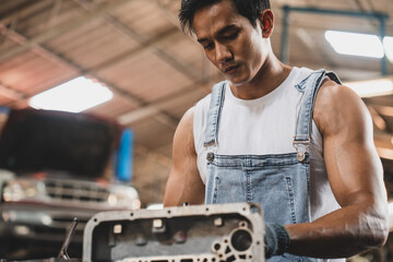 Handsome young male mechanic and car repair service man using various tools to repair engine motor wearing overalls and hand gloves in modern garage and maintenance workshop during daytime
