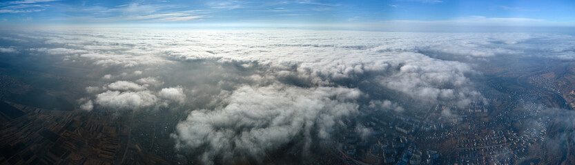 Aerial view from high altitude of distant city covered with puffy cumulus clouds forming before...