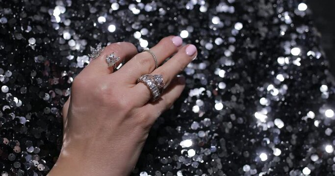 Video of close up elegant hand move fingers with sparkling gems and jewelry rings on black sparkling textile background