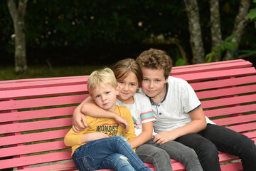 group of three happy children sitting on a red bench