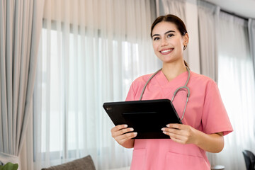 Young processional Caucasian Geriatric doctor in pink scrubs with stethoscope holding digital tablet. Physician in hospital nursing or wellbeing county. Happy caregiver taking care of elderly people.