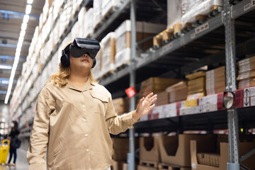 Plus size female worker inspecting box of products and use virtual reality technology for...