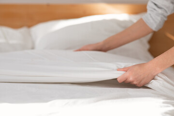 Hands of young european woman makes white bed with blanket in bedroom interior, close up