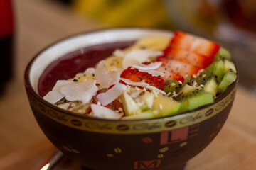An acai bowl with strawberry and kiwi, in a wooden table