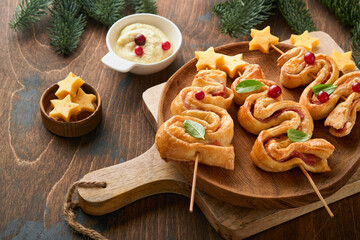Obraz na płótnie Canvas Christmas or New Year appetizer. Christmas tree shape puff pastry buns with cheese and ham. Group of Christmas tree shapes on wooden board. Festive idea for Christmas or New Year dinner. Top view.
