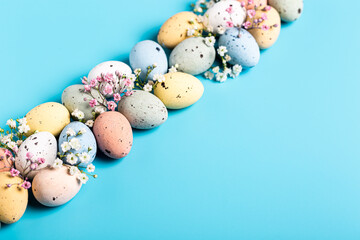 Easter composition with spring flowers and colorful quail eggs over blue background. Springtime and Easter holiday concept with copy space.