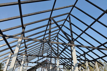 Steel roof structure. Detail of black steel truss structure for building construction on blue sky background and selective focus.