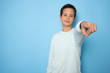 Boy looking and pointing to camera standing isolated over blue background.