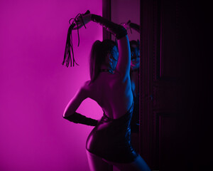 Sexy lover girl in latex bdsm costume and leather cat mask in neon light in front of the mirror - obrazy, fototapety, plakaty