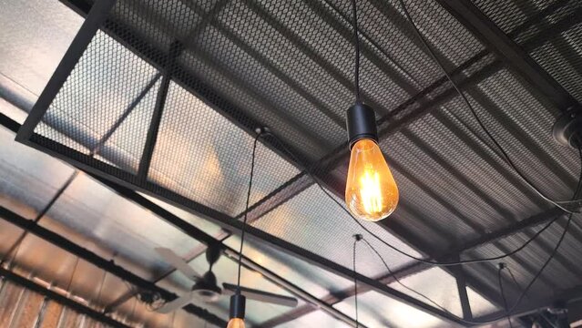 A classic style ceiling light bulb which is glowing in orange warm lighting shade. Interior object for room decoration. 4k footage with camera panning movement.