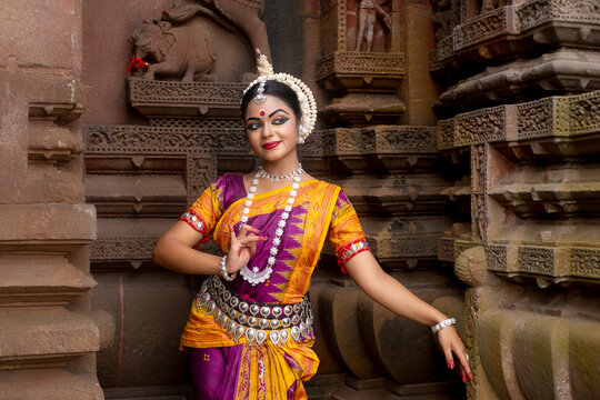Indian odissi dancer posing in front of temple sculpture 