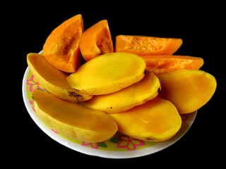 Sliced ripe mangoes and papayas on a plate, isolated on black background.