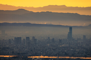 Fototapeta premium Haze layer over city by river and mountains with orange sunrise glow