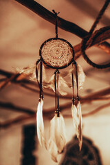 Fototapeta na wymiar Dreamcatcher hanging in boho beige interior in the evening light. Magical and ritual ornament. Vertical