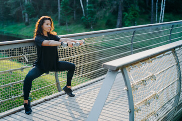 Horizontal shot of brunette woman excersises with dumbbells, does squats, dressed in active wear, poses at bridge, being motivated, has workout exercises, leads sporty lifestyle. Fitness, workout