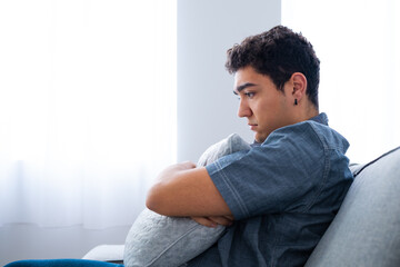 Sad hispanic boy hugging pillow. Pensive teenager suffering depression.