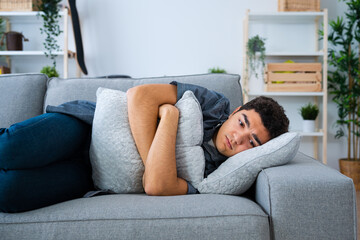 Depressed hispanic teenager boy lying on sofa. Sadness, depression and anxiety concept