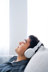 Hispanic teenager boy listening to music on headphones with closed eyes.