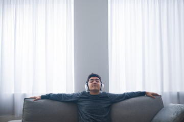Hispanic teenager boy listening to music and relaxing on sofa with copy space