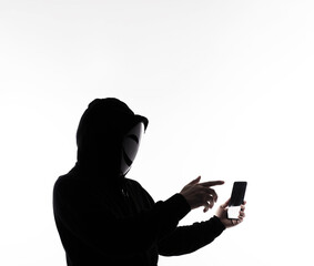 Hacker Anonymous and face mask with smartphone in hand. Man in black hood shirt holding and using...