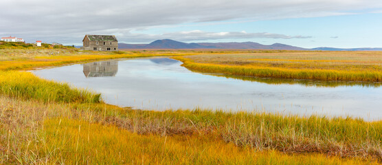 Tundra landscape in autumn colors with river, ruin of an old wooden house from the goldrush era and...