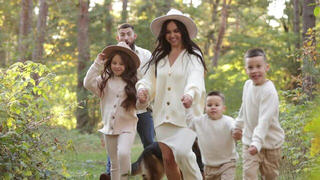 Happy playful family runing in park with pet. Young mom, dad having fun with three kids and big dog outdoors. Parents with children holding hands. Active lifestyle parenthood concept. Happy childhood