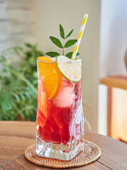 Glass of cold fresh cocktail with citruses and straw garnished with green leaves and placed on table in daytime