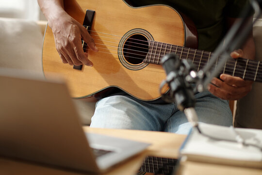 Closeup image of artist playing guitar at home and recording sound with microphone