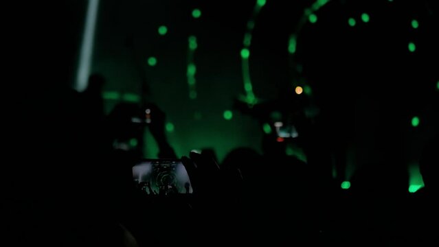 People hands silhouette taking photo or recording video of live music concert with smartphone. Bright colorful green stage lighting. Nightlife, technology, photography, entertainment concept