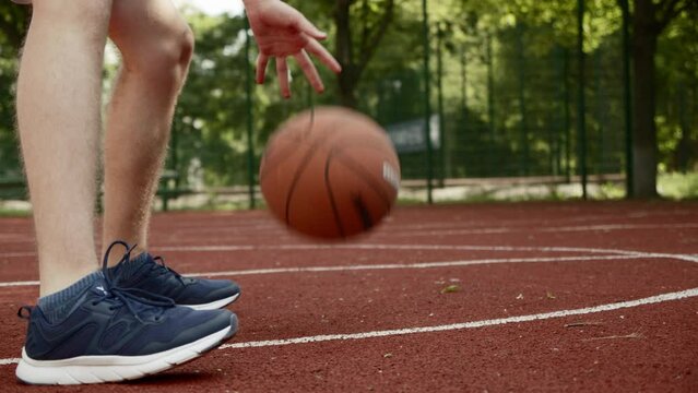 Footage of a teenager dribbling on an outdoor court, during a bright and sunny summer day. Video of a white caucasian teen training to play basketball.