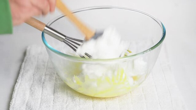 Man transfers whipped meringue egg whites to bowl with ready-made dough made from flour and egg yolk. High quality 4k footage