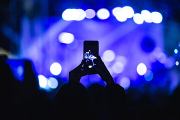 Fototapeta na wymiar Person holding smartphone and silhouettes of concert crowd with stage lights