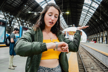 young woman standing on the train platform outraged, waiting and seeing the time on the clock.