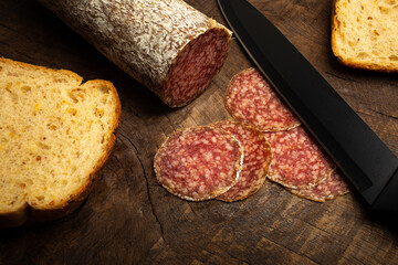Hungarian salami with grain bread slices on a rustic old wooden background.