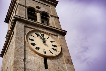 clocktower or belltower of old stone church building, typical clock face with roman numerals