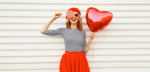 Portrait of happy smiling woman with red heart shaped balloon wearing beret and skirt on white...