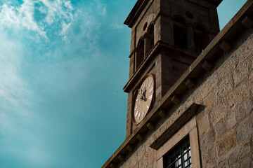 Fototapeta na wymiar clocktower or belltower of old stone church building, typical clock face with roman numerals