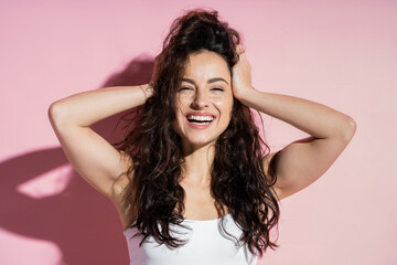 Fototapeta premium Cheerful freckled woman touching hair on pink background.