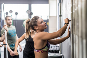 Fototapeta na wymiar Athlete woman writing down exercises on the gym blackboard making plan for training