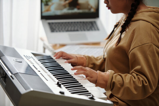 Closeup image of girl playing new song on synthesizer when having online class
