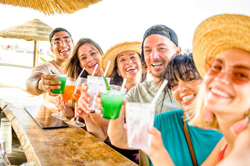 Happy multi ethnic friends cheering and drinking coloured cocktails in kiosk at beach - Young...
