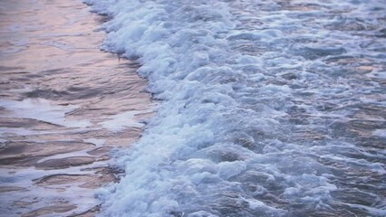Unsettling sea water reflects pink sunlight as foamy wave washes over