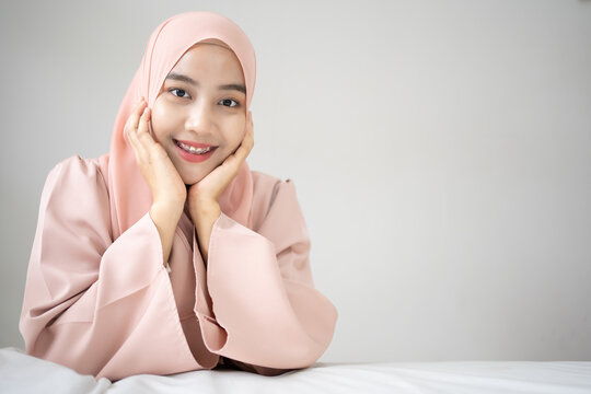 Asian Muslim woman lying at the bed underneath the quilt and smiling, with her smile dental care.